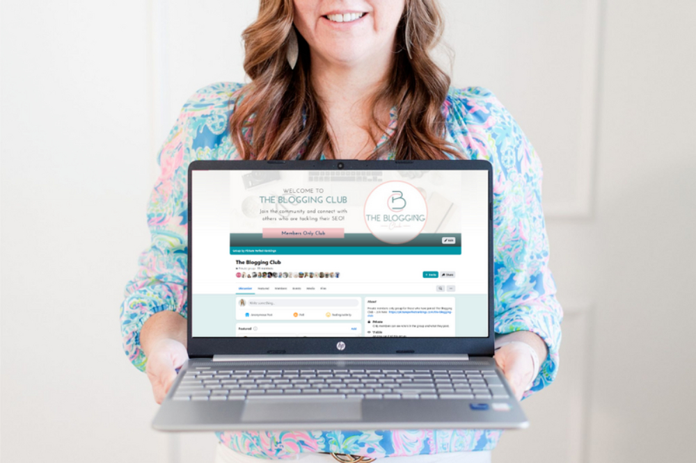 A smiling person holds a laptop displaying an online blogging community page. The bright, friendly scene emphasizes digital connection, content creation, and consistent marketing through community engagement and online platforms.